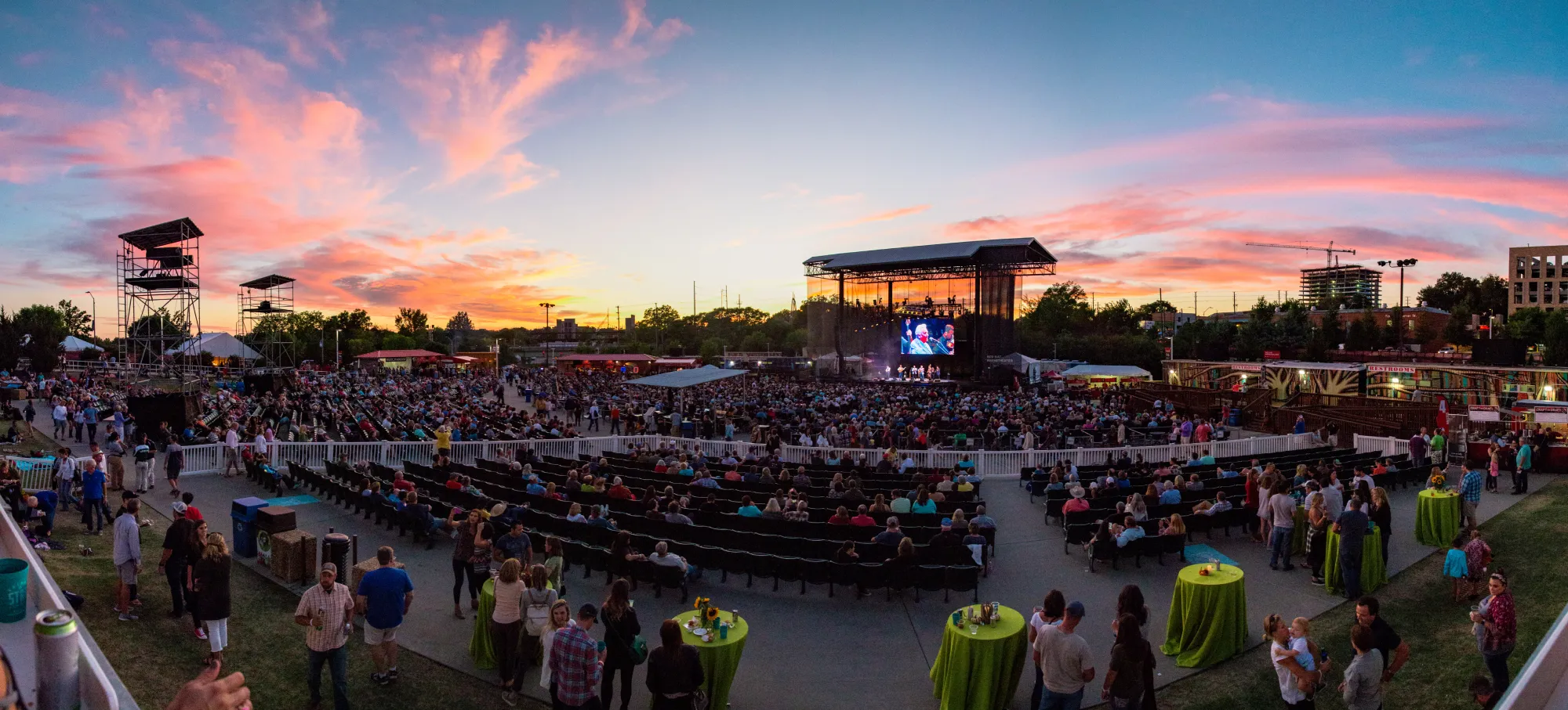 An outdoor amphitheater with a crowd of people and a stage at sunset.