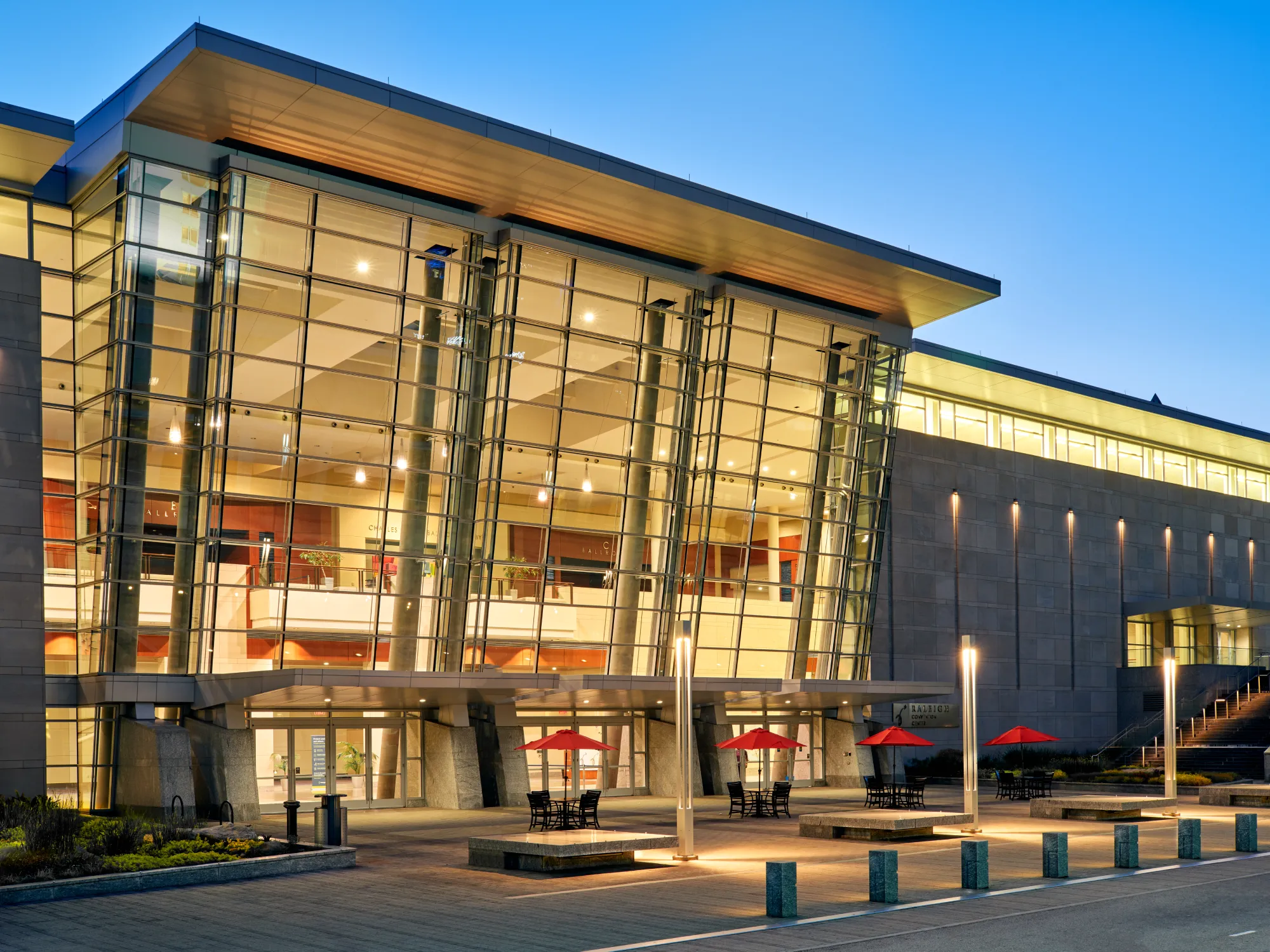 Large modern building with glass walls and red umbrellas in front.