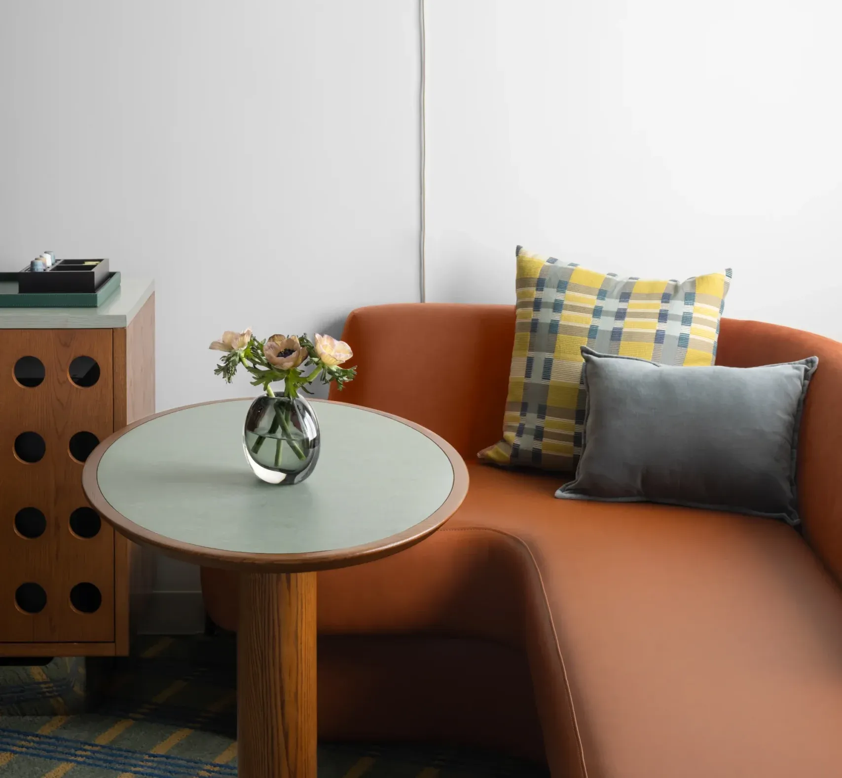 A small table with a vase of flowers on it, accompanied by a couch with a throw pillow, set against a white wall with a hanging light fixture.
