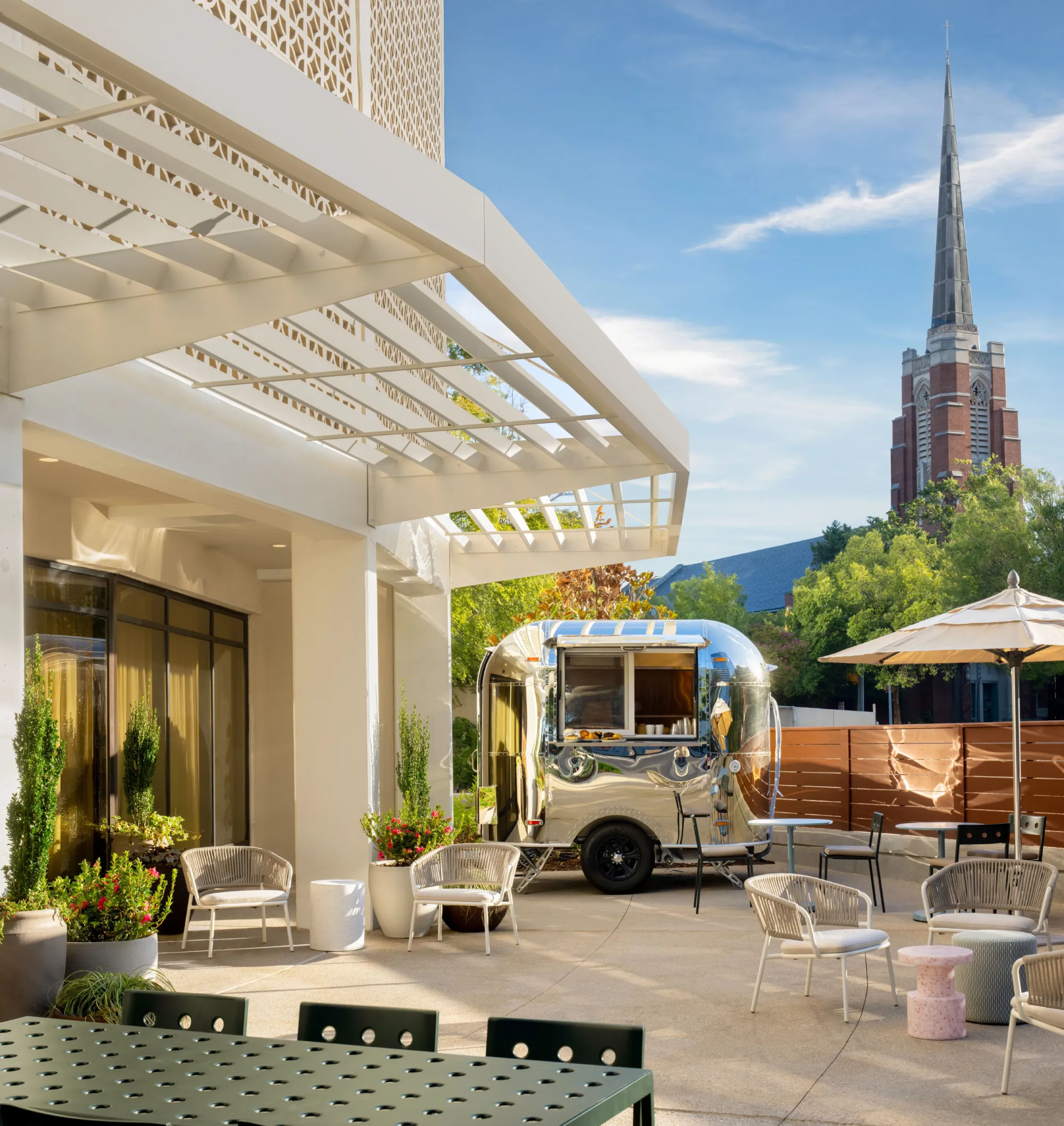 The mirror-polished vintage Airstream coffee bar in the courtyard of Hotel Indigo Raleigh Downtown, under a white canopy pergola