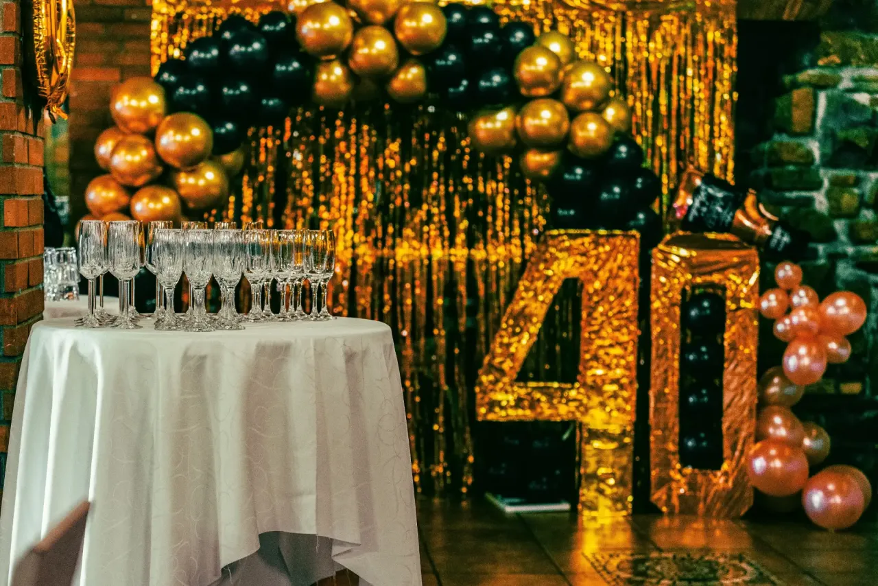 Champagne flutes on a table in front of a gold and black balloon celebration display