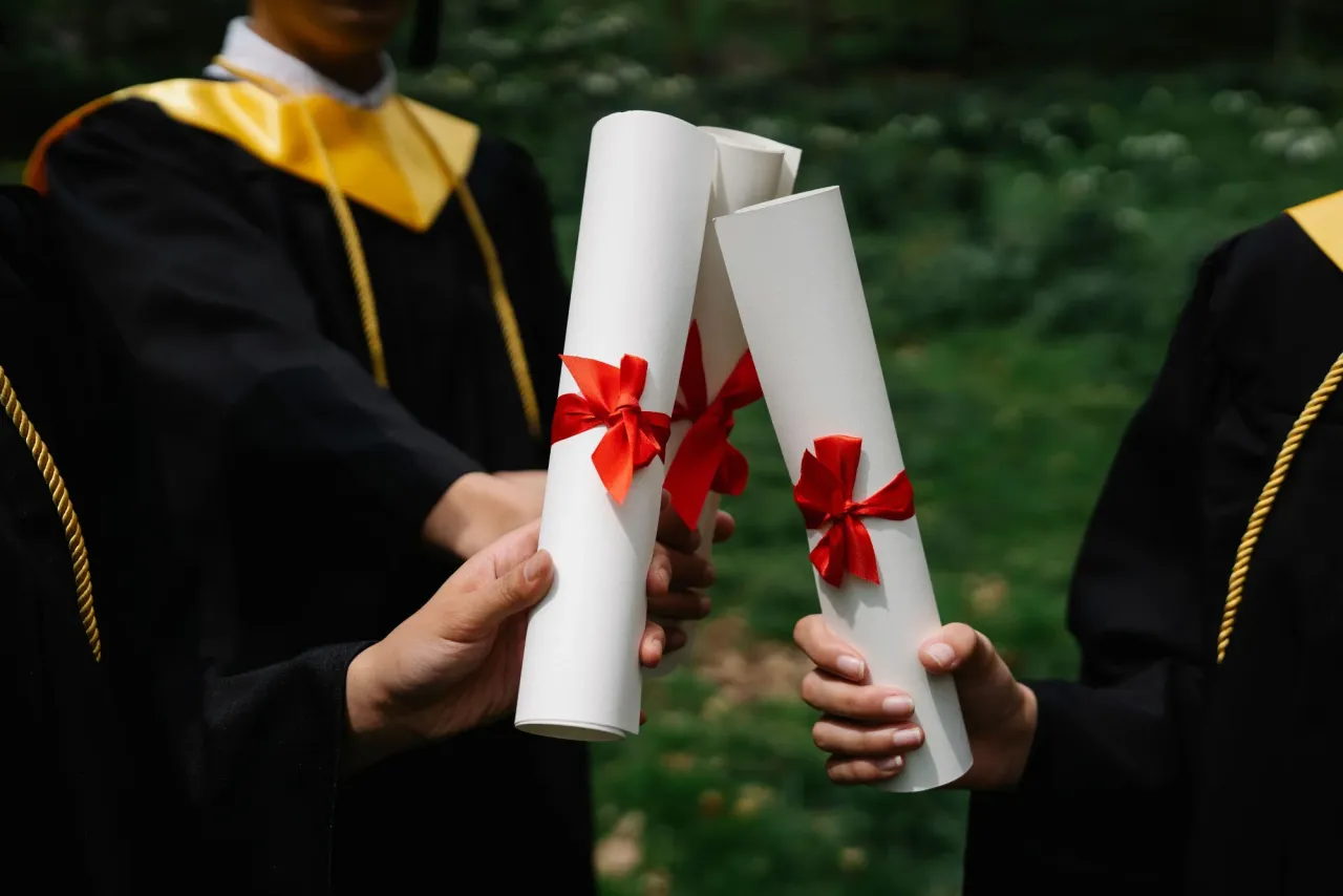 Graduates in gowns holding diploma scrolls tied with red ribbons