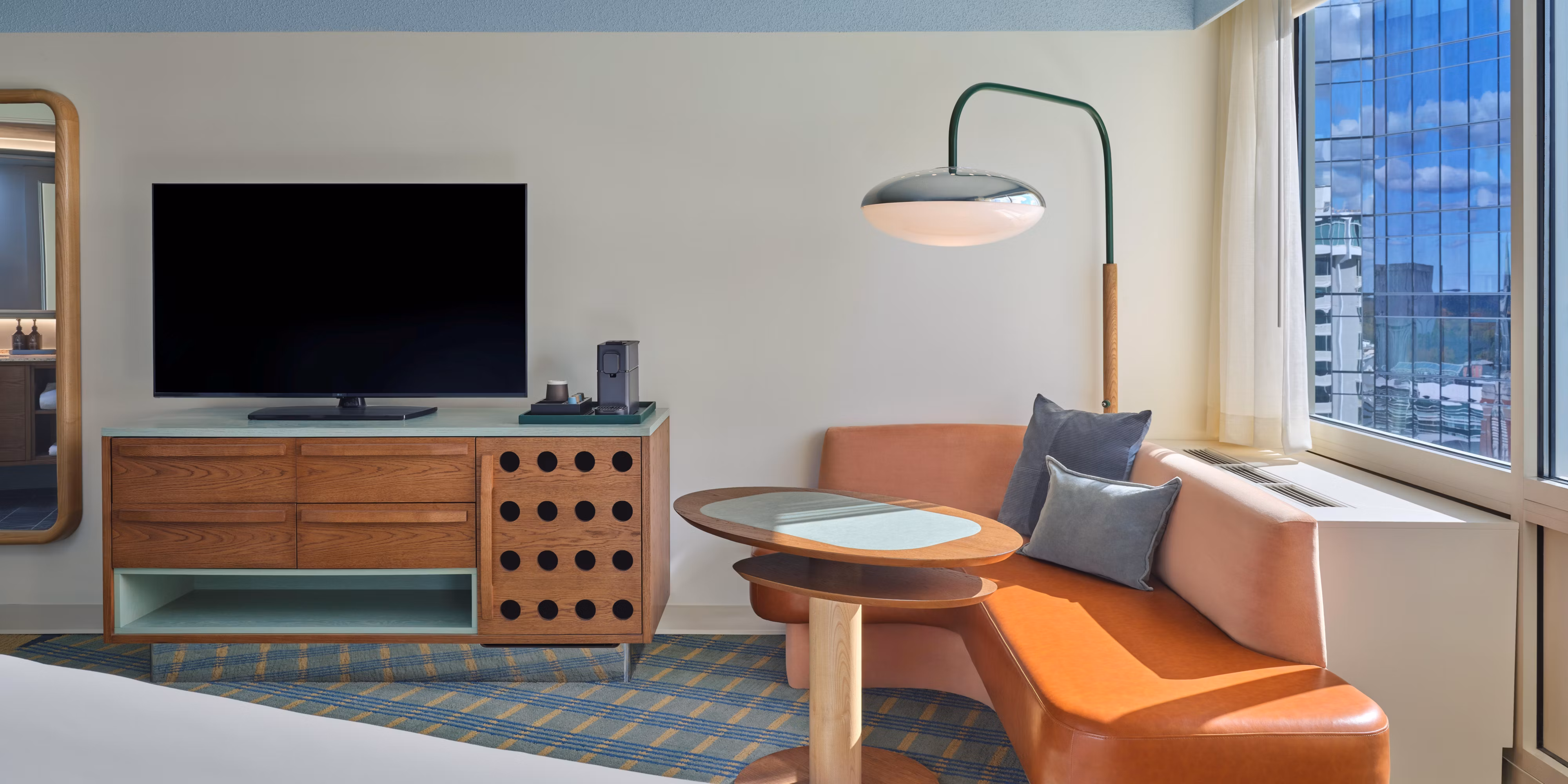 King guest room at Hotel Indigo Raleigh Downtown with a curved orange leather sofa and skyline views