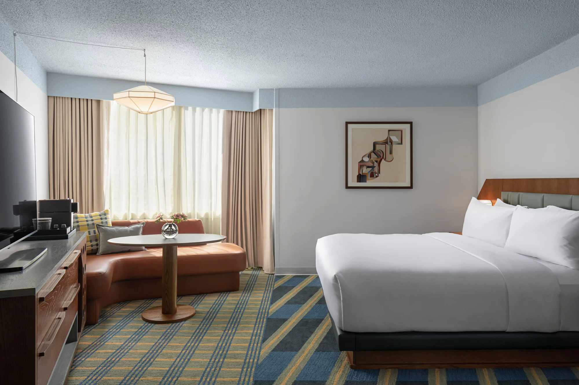 Standard King room at Hotel Indigo Raleigh Downtown with a king bed, curved lounge seating, a table for two and a flat-screen TV